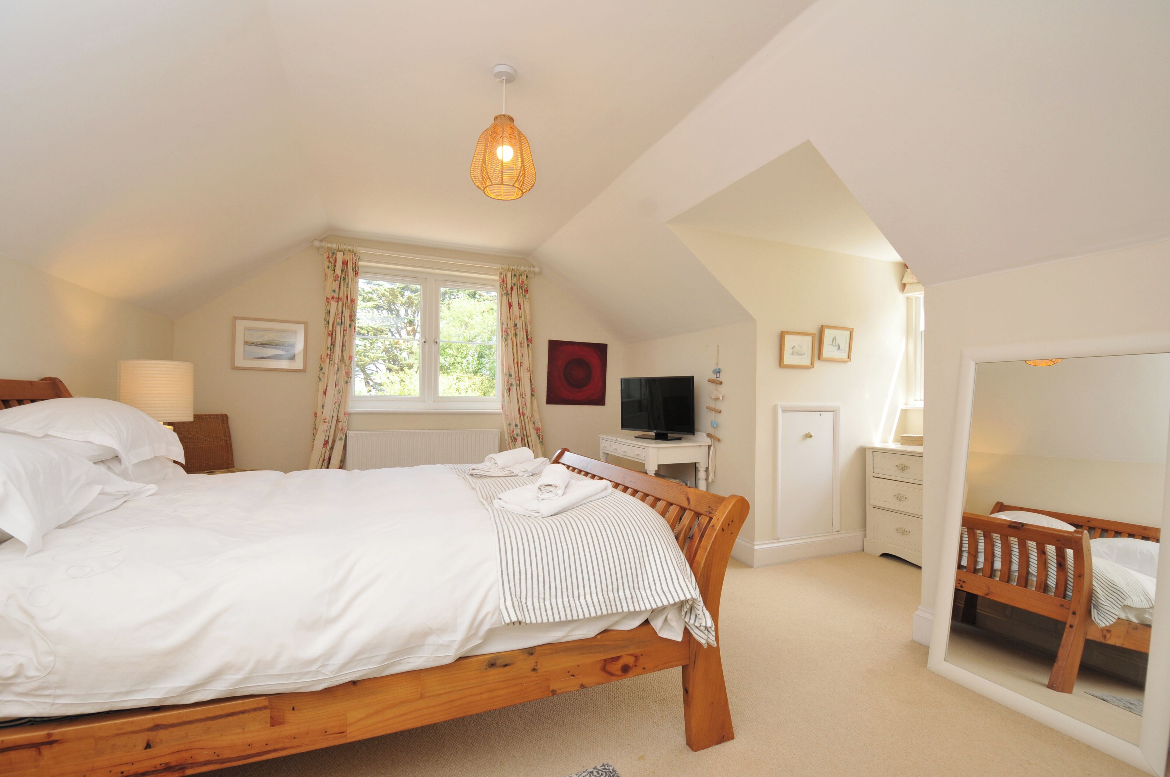 A bedroom with a wooden bed, a desk with a television, a window with curtains, and a mirror.