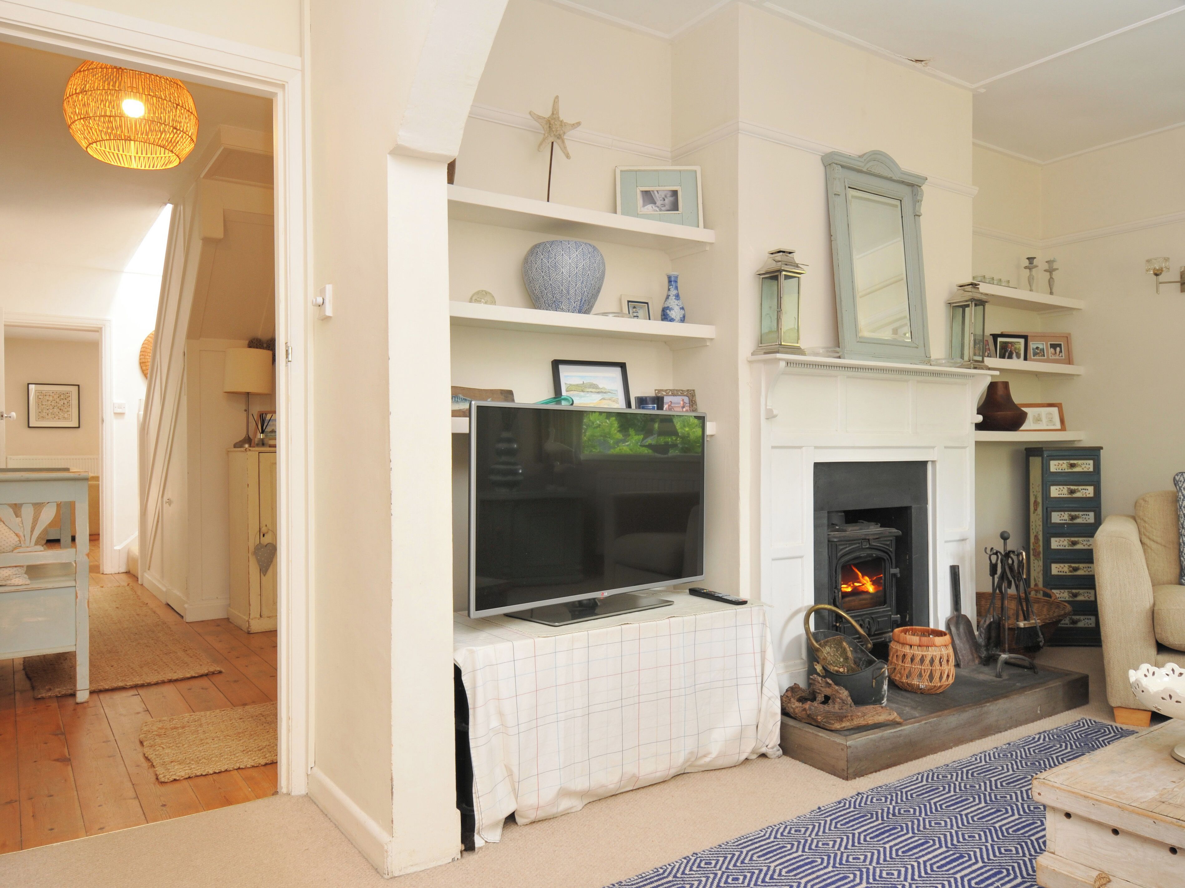 A living room with a fireplace, television, and decorative items on shelves.