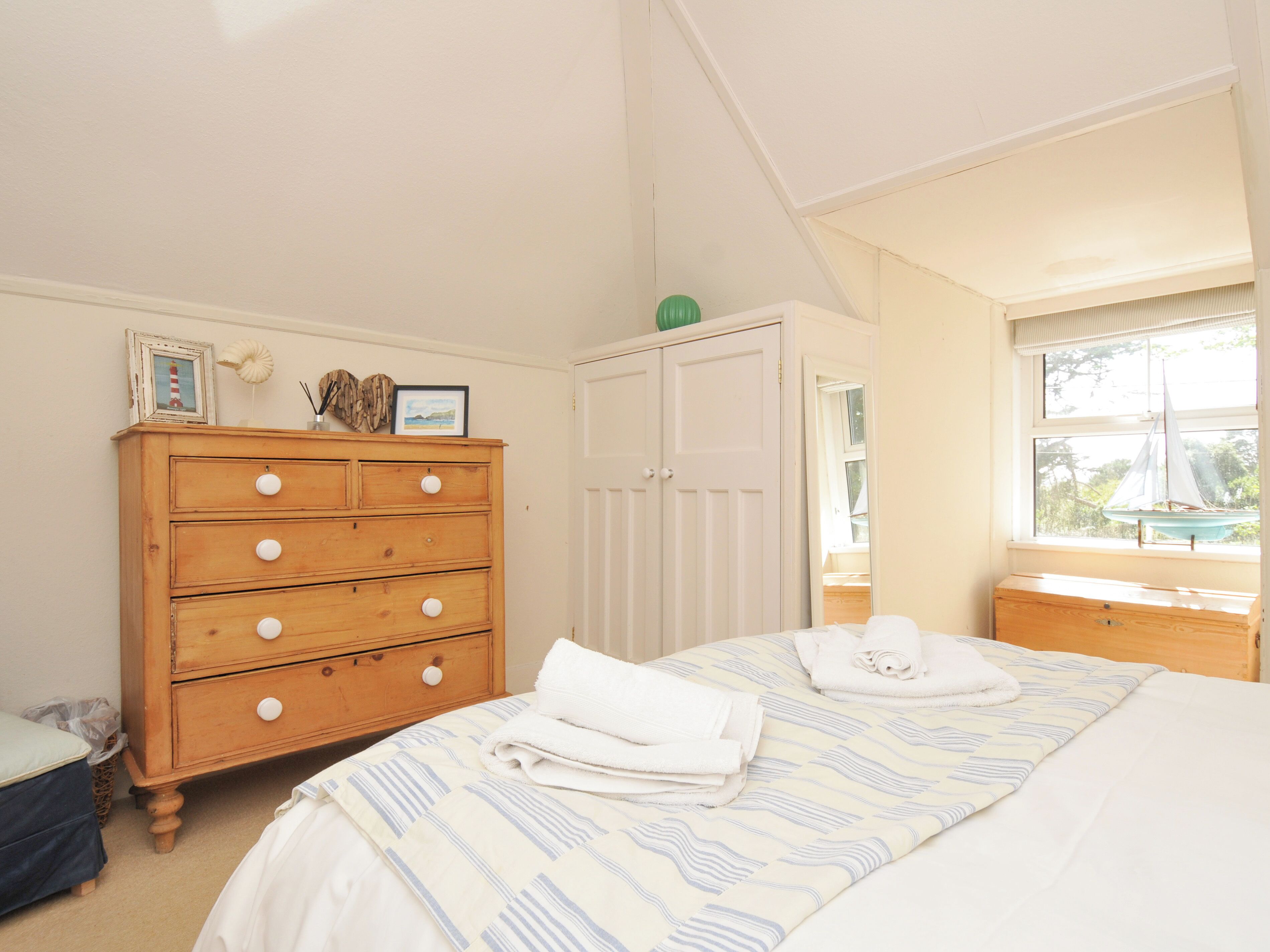 Une chambre à coucher avec un lit, une commode en bois, une armoire et une fenêtre donnant sur un voilier.