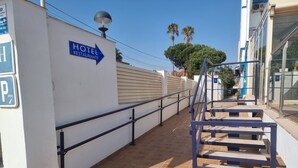 A hotel entrance with a sign indicating a restaurant direction, a parking sign, and a staircase leading to a covered area. - Hotel Aloha (Burriana)