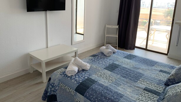 A hotel room with a bed, a TV, a desk, a chair, and a window with curtains. - Hotel Aloha (Burriana)