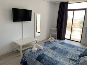 A hotel room with a bed, a TV, a desk, a chair, and a window with curtains. - Hotel Aloha (Burriana)