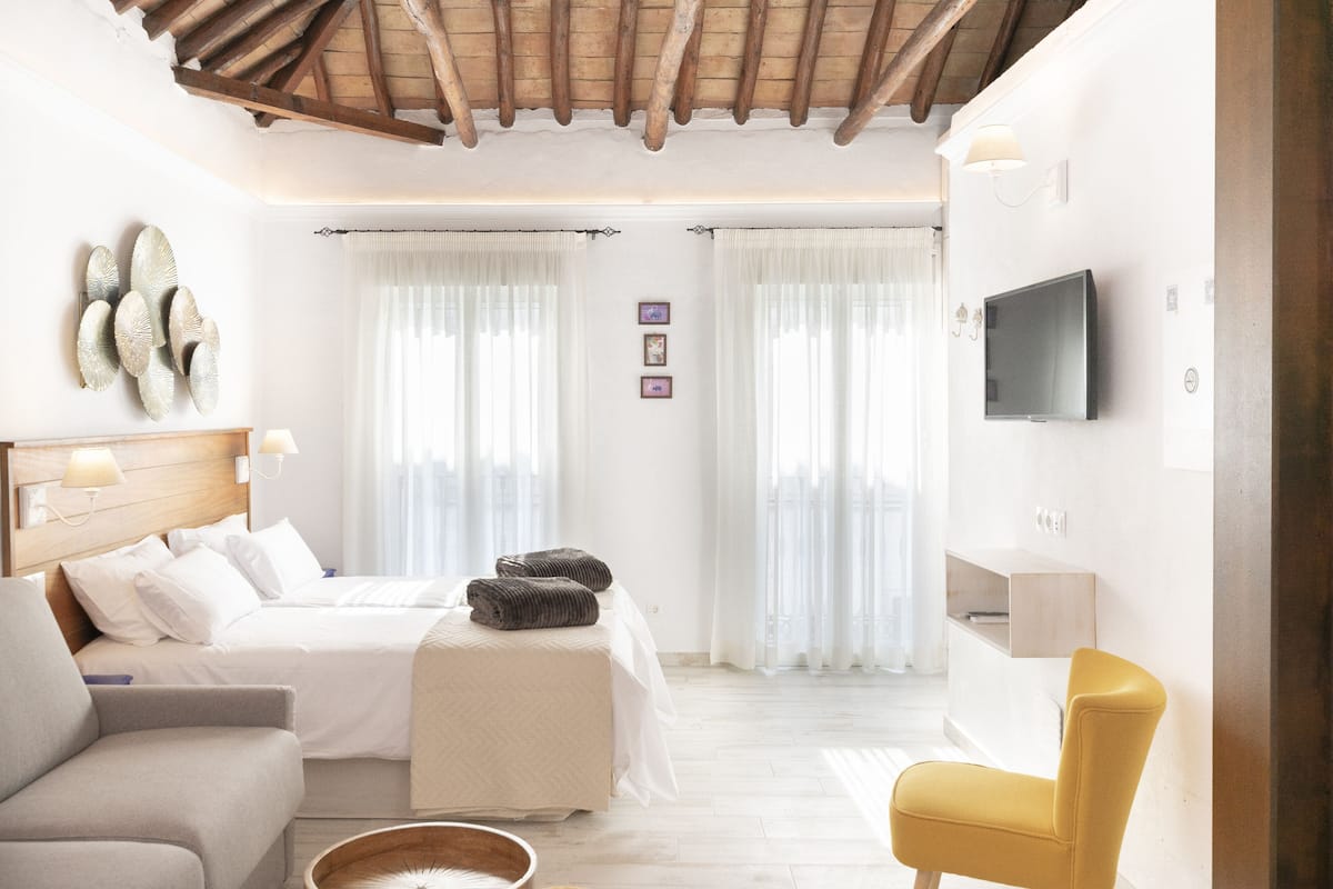 Una habitación de hotel moderna con cama, sofá, sillón, televisión y techo de madera.