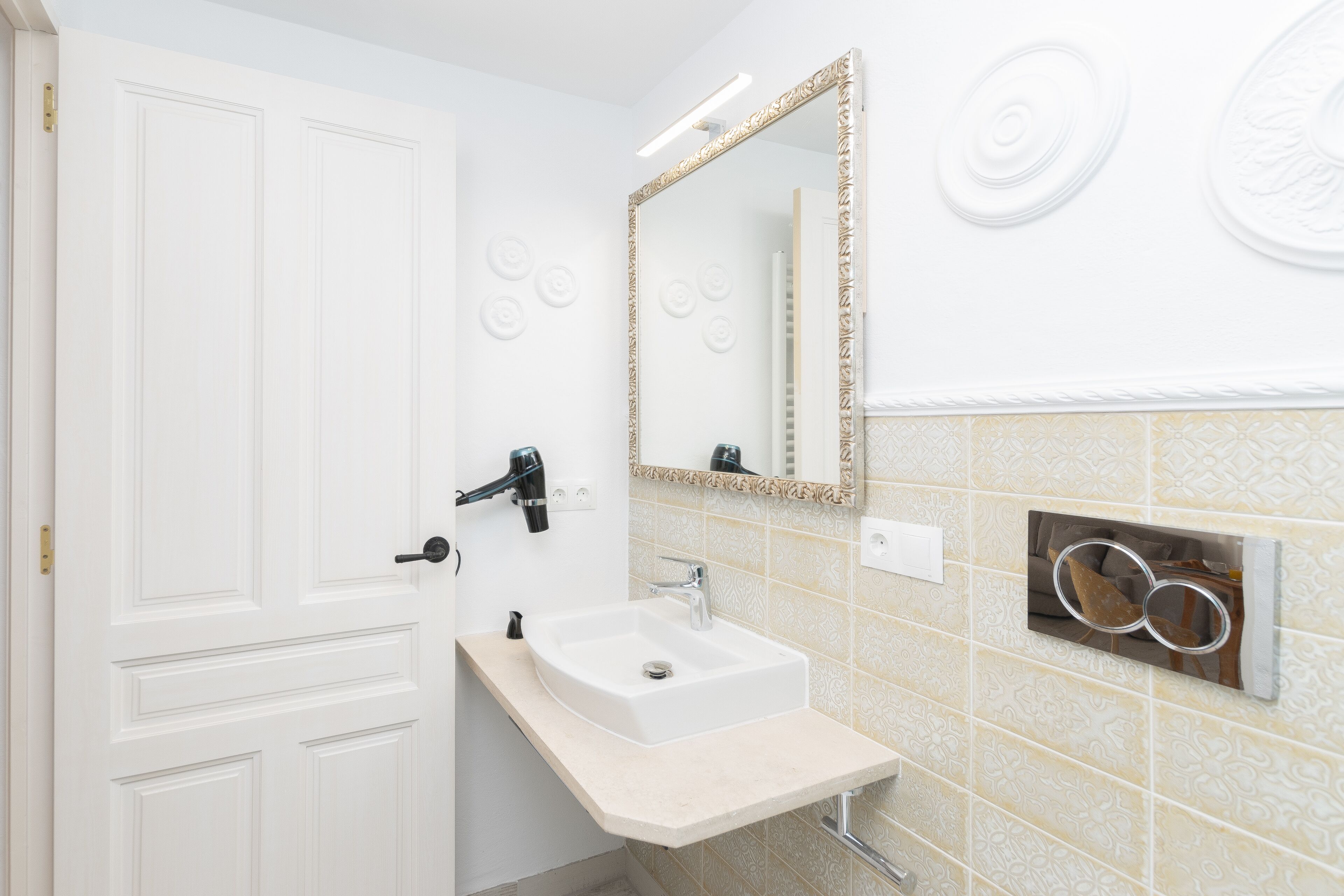 A bathroom with a white door, a sink with a mirror, and decorative wall tiles.