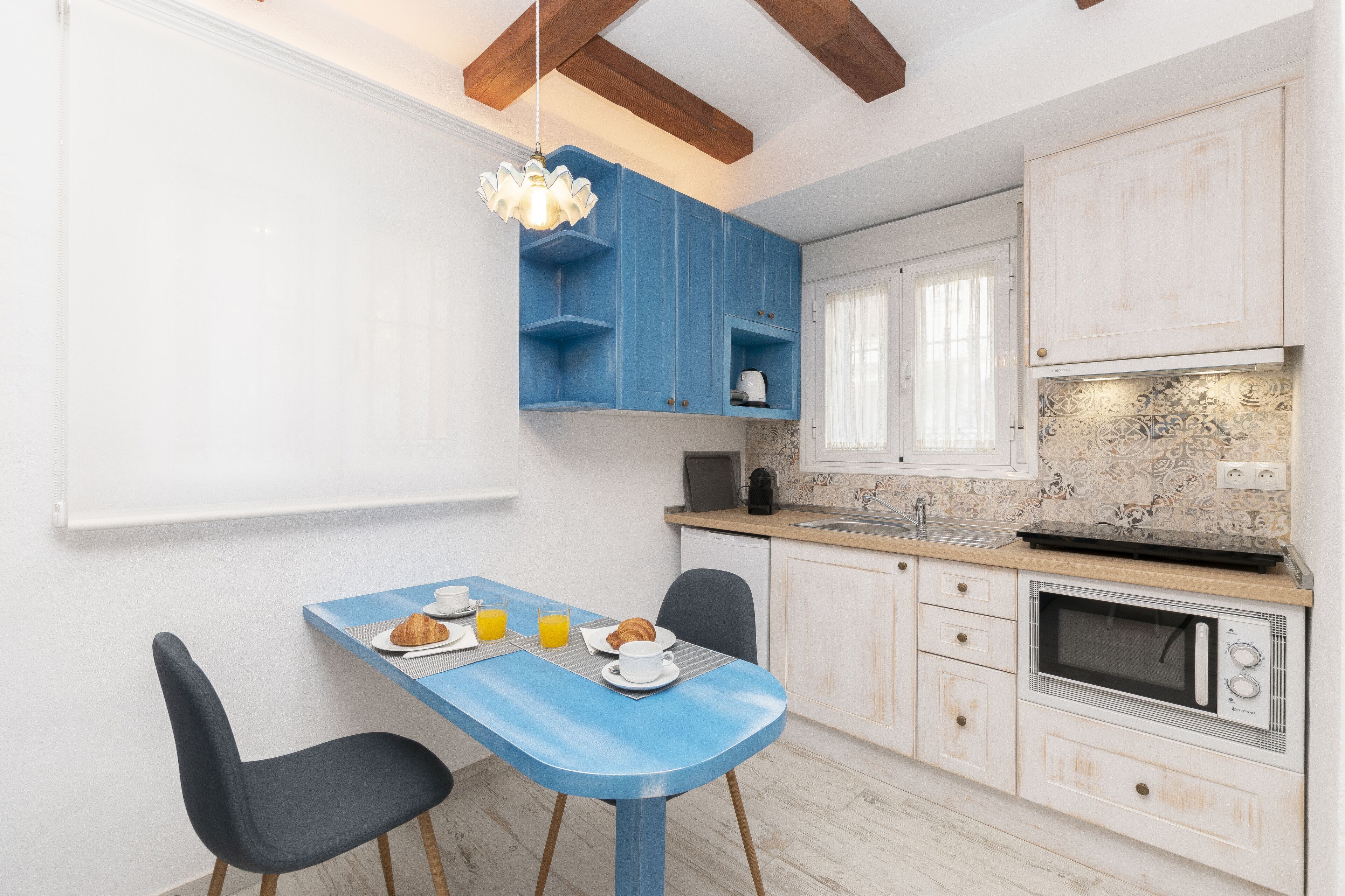 A modern kitchen with blue cabinets, a microwave, and a dining area with a blue table and chairs.