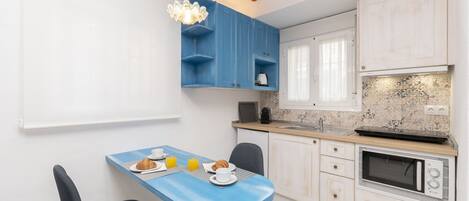A modern kitchen with blue cabinets, a microwave, and a dining area with a blue table and chairs.