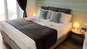 Uma cama bem arrumada com travesseiros e coberta, uma luminária de cabeceira e uma mesinha com abajur.