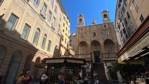 Uma praça histórica com uma fonte central, cercada por arquitetura clássica e um mercado com vendedores.