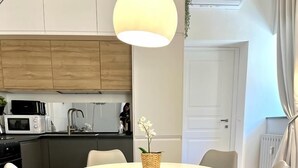 Uma cozinha moderna com armários brancos, micro-ondas e pia. Há uma área de refeições com uma mesa redonda e quatro cadeiras.