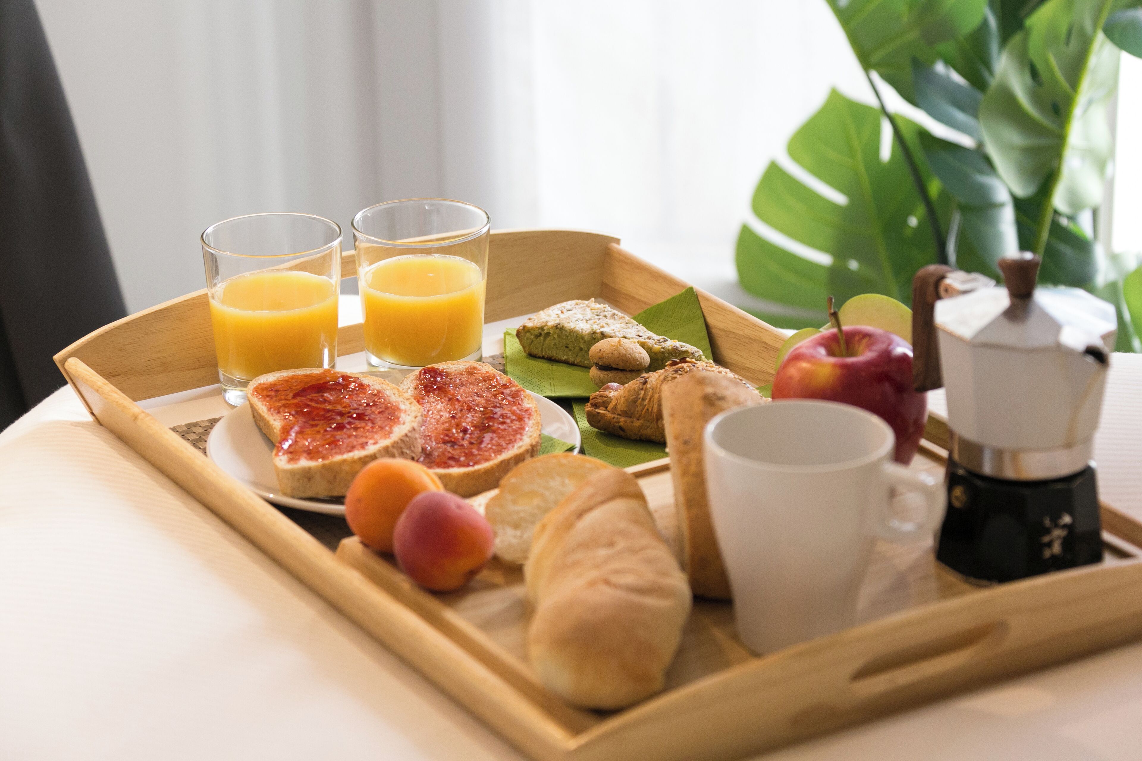 En bakke med morgenmad, bestående af ristet brød, marmelade, kager, frugt og en kaffemaskine.