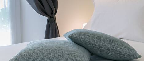 A bed with two patterned pillows, a dark curtain, and a white wall with a decorative molding.