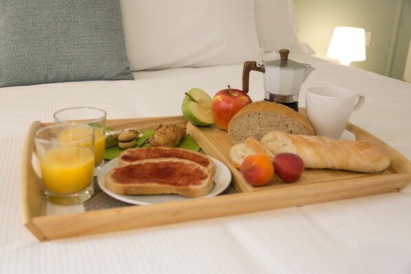 Bandeja de desayuno con tostadas, fruta, jugo y una cafetera sobre la cama.