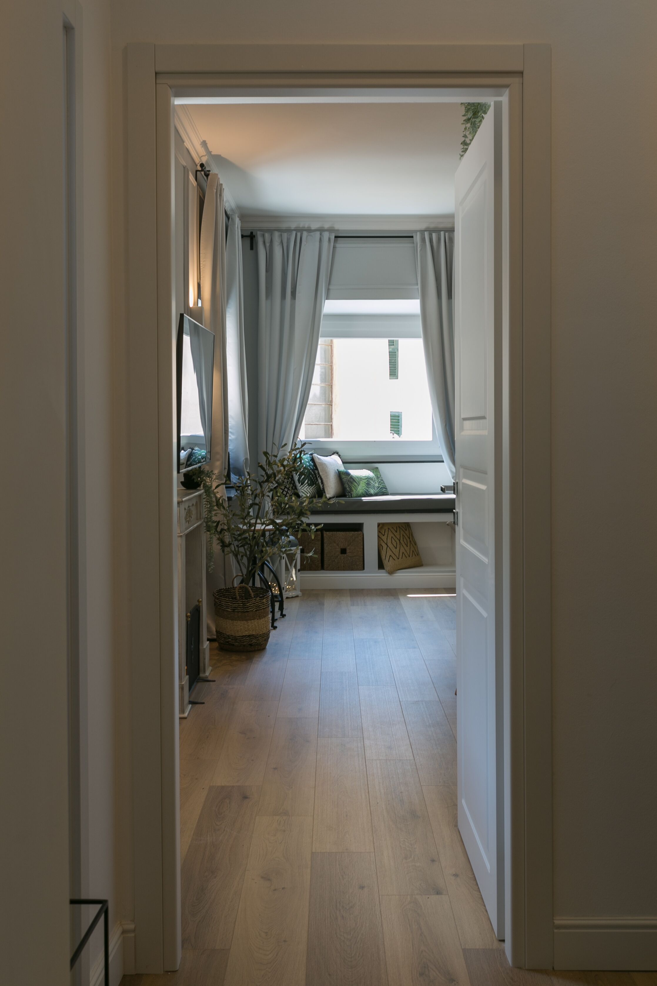 A hallway leading to a room with a window, a bench, and a potted plant.