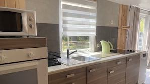 A modern kitchen with a microwave, stove, sink, and a window with blinds. - Nature lovers by the sea (Bormes-les-Mimosas)