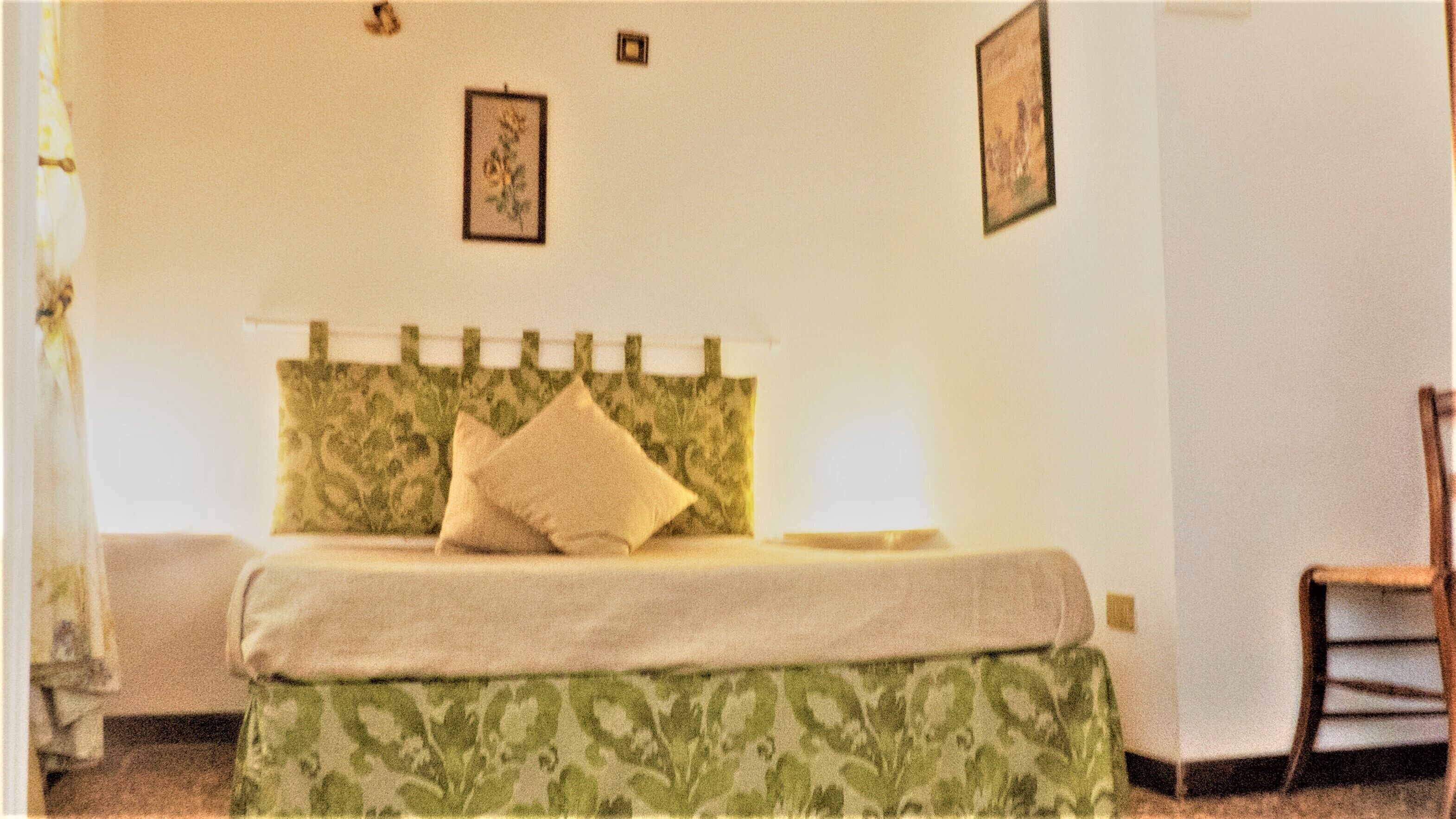 A bedroom with a bed, a chair, and two framed pictures on the wall.