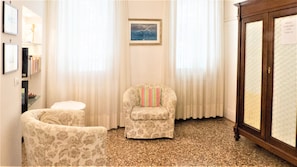 Ein Zimmer mit einem blumengemusterten Sessel, einem kleinen runden Tisch und einer Kommode mit einer gesteppten Oberfläche.