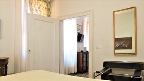 Ein Hotelzimmer mit einem Bett, einem Sessel, einem Schreibtisch, einem Spiegel und einer Tür zu einem anderen Raum.