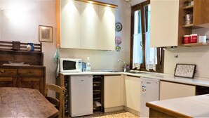 Eine kompakte Küche mit Mikrowelle, Spüle und kleinem Kühlschrank. Ein Holztisch und ein Stuhl sind vorhanden.