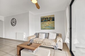 Una sala moderna con una mesa de centro de madera, un sofá, un cuadro en la pared, un reloj y una ventana con cortinas.