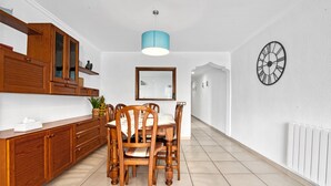 Un coin repas comprenant un buffet en bois, une table avec des chaises, un luminaire suspendu, une horloge murale et un radiateur.