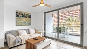 Un salon moderne comprenant un canapé, une table basse, un ventilateur de plafond, un tableau et une porte-fenêtre coulissante donnant sur une terrasse extérieure.