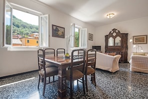 Zona pranzo con tavolo e sedie in legno, vista su una collina attraverso una finestra e un ampio mobile in legno.