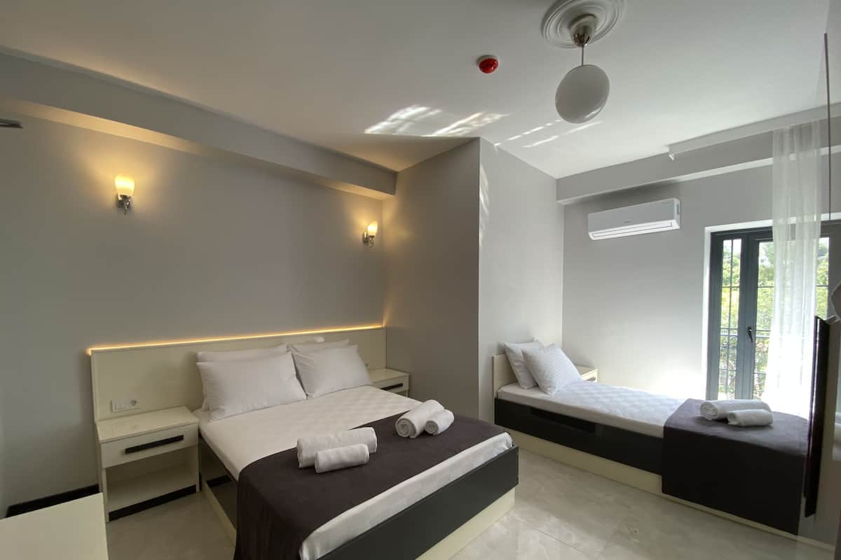 A modern bedroom with a large bed, bedside tables, a ceiling light, and a window with curtains.