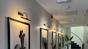 Un pasillo con fotografías blanco y negro enmarcadas en la pared, una planta en maceta y una escalera al fondo.