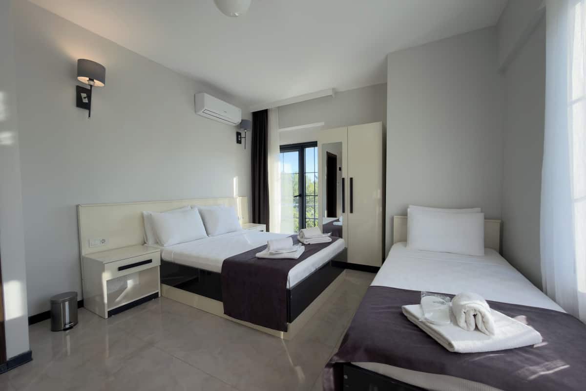 A hotel room with two beds, a small desk, a trash bin, and an air conditioning unit.