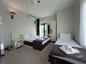 A hotel room with two beds, a small desk, a trash bin, and an air conditioning unit.