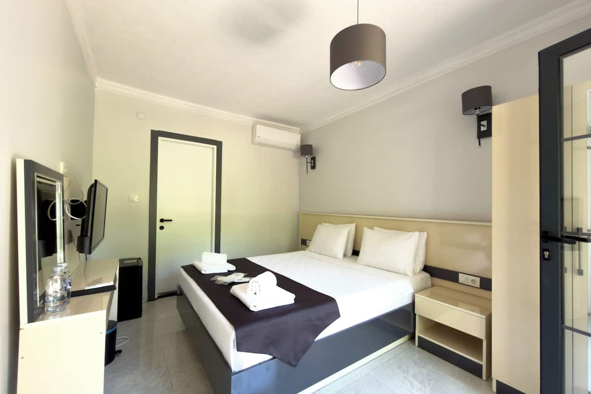 A hotel room with a bed, bedside table, a mirror, a TV, and a door.