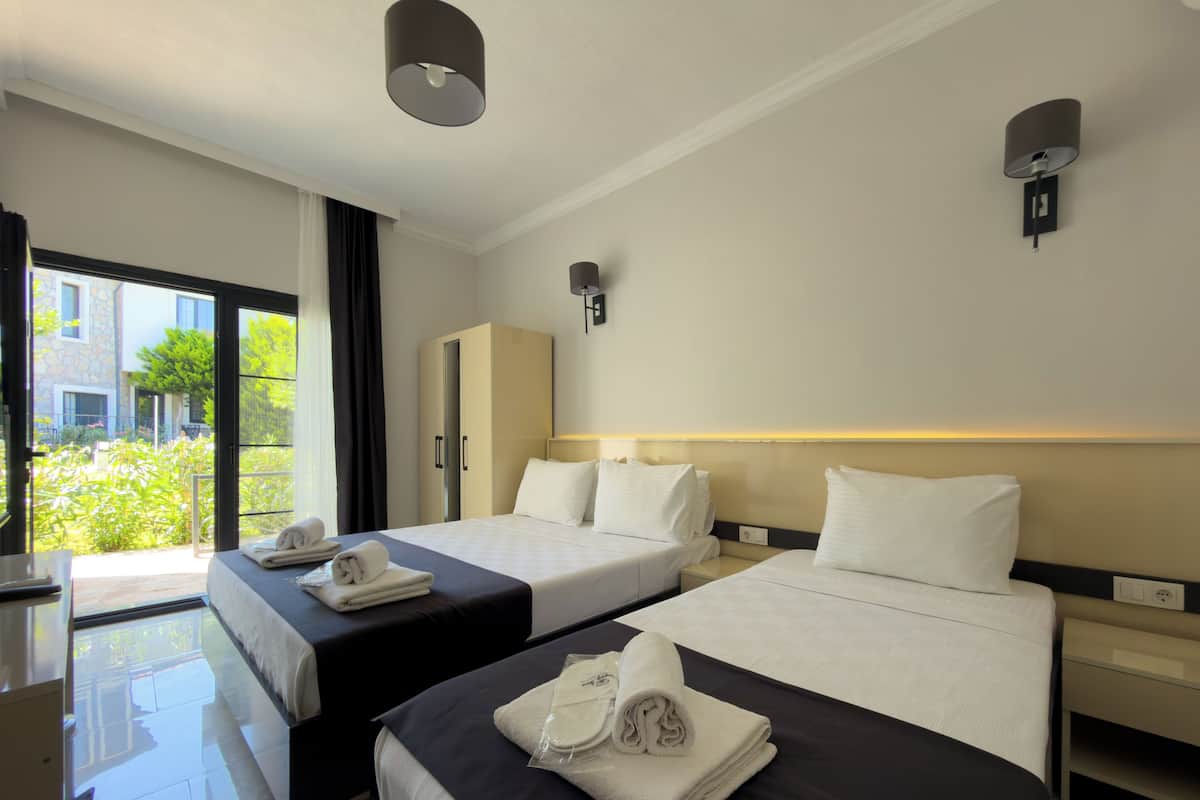 A hotel room with two beds, a wardrobe, a desk, and a view of greenery outside.