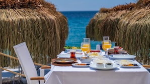 Una mesa lista para el desayuno con vista al océano, rodeada de sombrillas de paja.