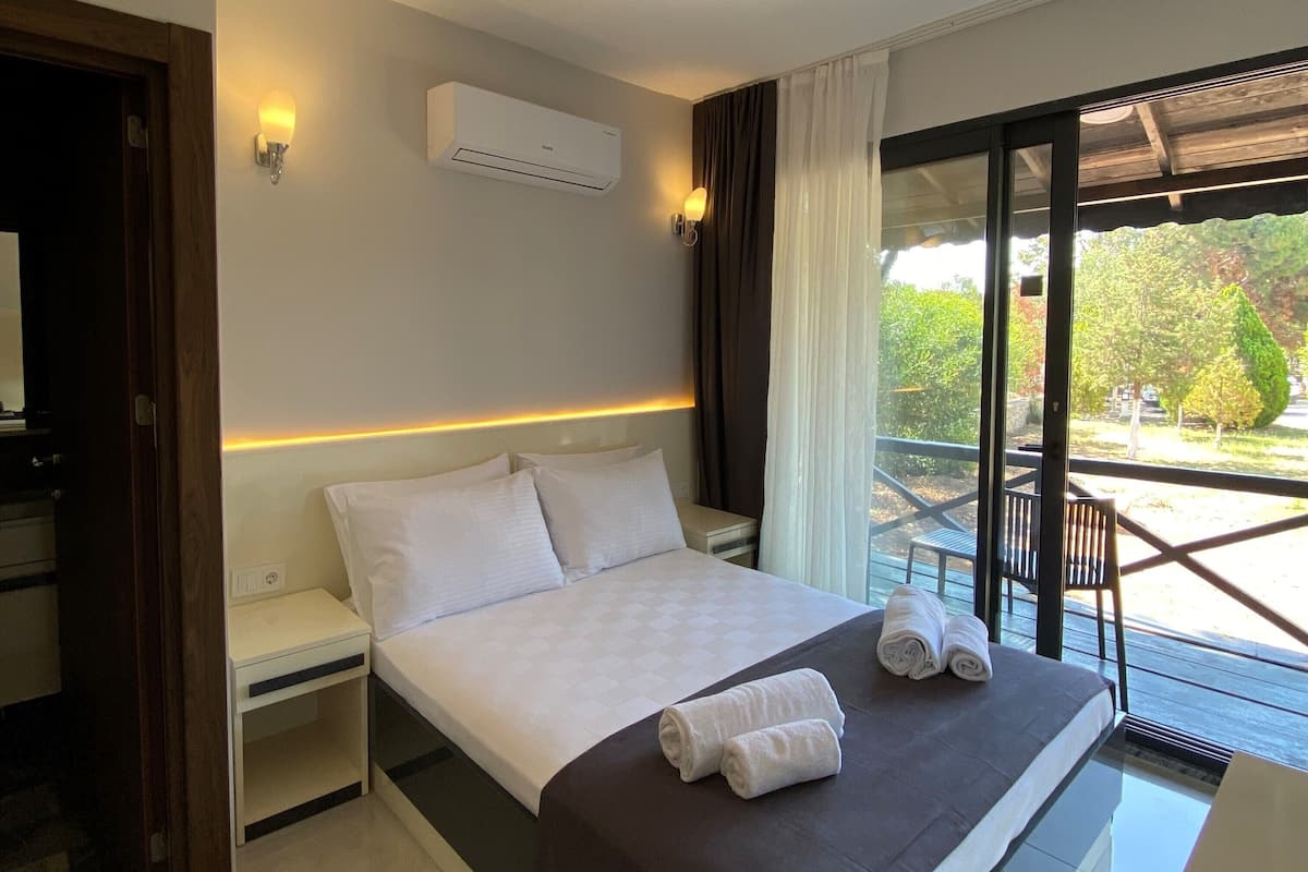 A modern hotel room with a large bed, a built-in air conditioner, a bedside table, and a view of the outdoors.