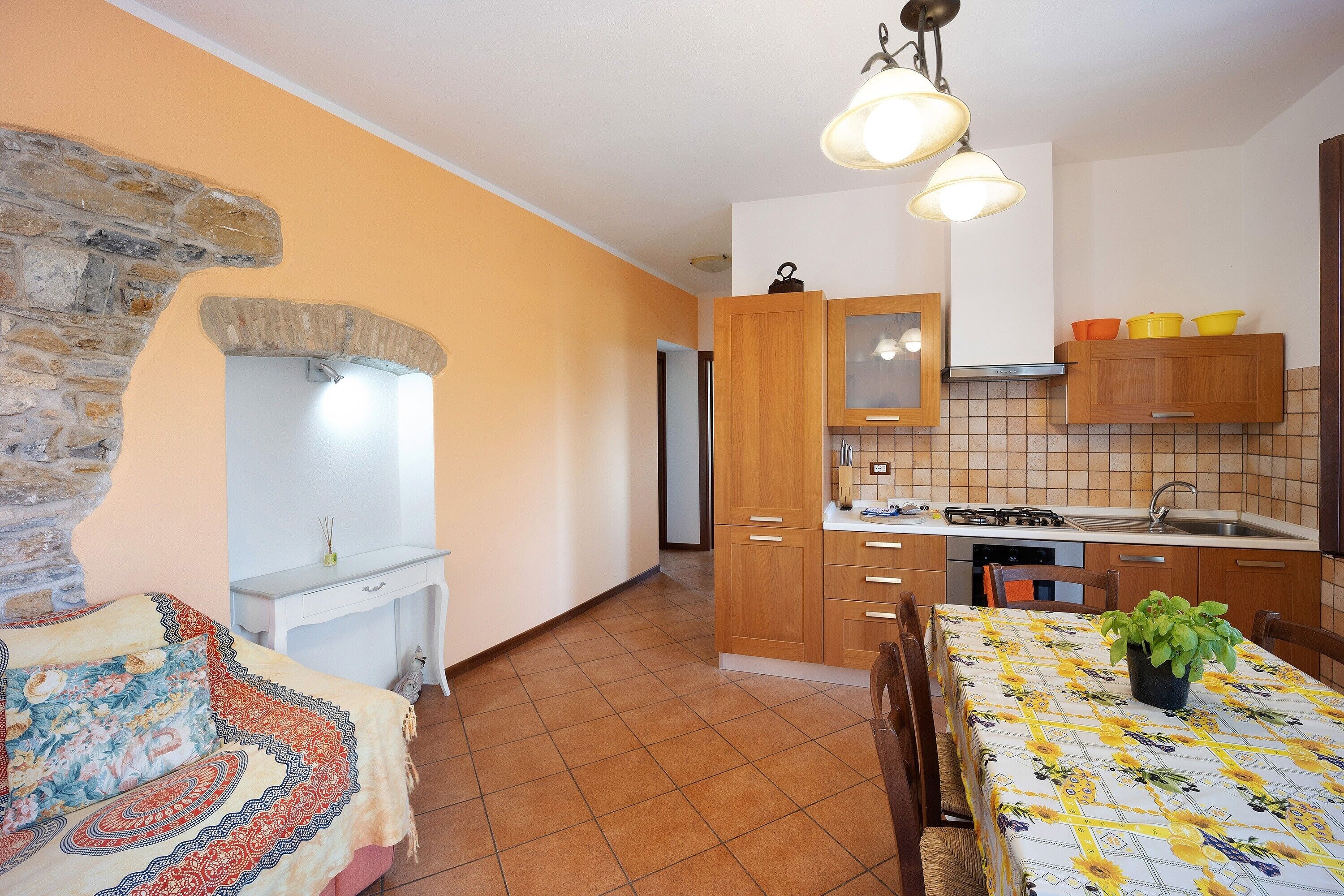 A kitchen with wooden cabinets, a tiled backsplash, and a dining table with a floral tablecloth.