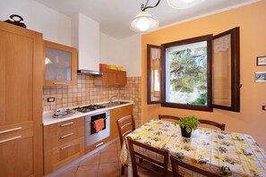 Une cuisine avec des meubles de rangement en bois, une cuisinière et une table à manger agrémentée d’une plante.