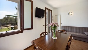 Un comedor con una mesa de madera, sillas, un florero con flores, un televisor en la pared y un sofá.