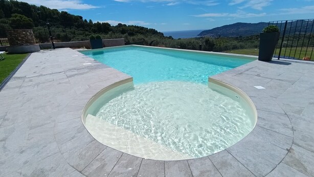Una piscina rectangular con un jacuzzi circular en el centro, rodeada por una terraza empedrada.