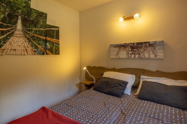 Un lit avec une couvre-lit à pois, un plaid rouge et une tête de lit dotée d’un luminaire.