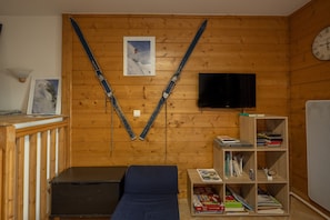Une pièce aux murs en bois, avec un téléviseur fixé au mur, une bibliothèque et un canapé bleu.