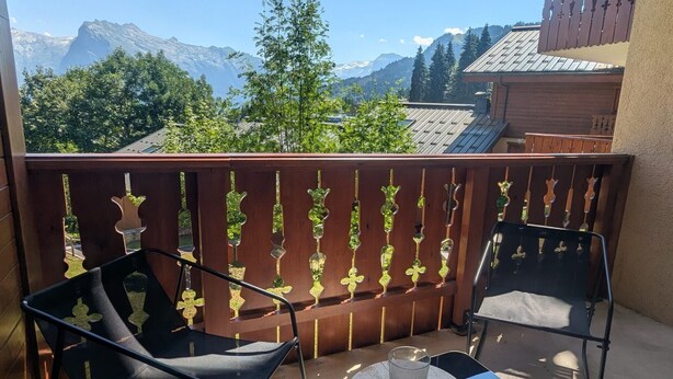 A balcony with two chairs and a table, a wooden fence with decorative elements, and a mountain view. - Apartment 'Morrillon 1100 Ski-in/Ski-out' with Mountain View, Balcony and Wi-Fi (Morillon)