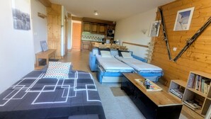 A room with a sofa, a bed, a desk, a bookshelf, and a kitchen area. - Apartment 'Morrillon 1100 Ski-in/Ski-out' with Mountain View, Balcony and Wi-Fi (Morillon)