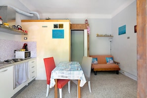A compact kitchen with a microwave, stove, and cabinets, a dining table with chairs, and a small sofa with cushions.