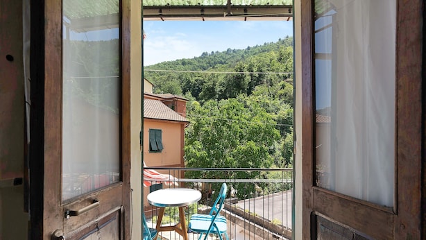 A balcony with a table and chairs, a view of a hillside, and a building in the background.