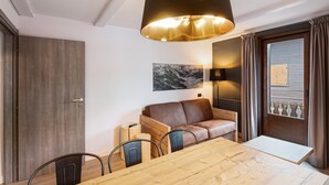 Ein Zimmer mit Esstisch aus Holz, einer Ledersofa, einer Holztür und einem großen Fenster mit Vorhängen.