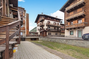 A traditional wooden building with balconies, a stone wall, and a paved area.