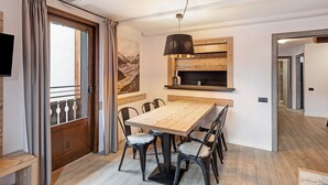 Ein Essbereich mit einem Holztisch und Stühlen, einer Hängelampe und einer Holzwand mit einem Bild.