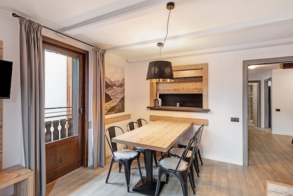 A dining area with a wooden table and chairs, a hanging light fixture, and a wooden wall with a picture.