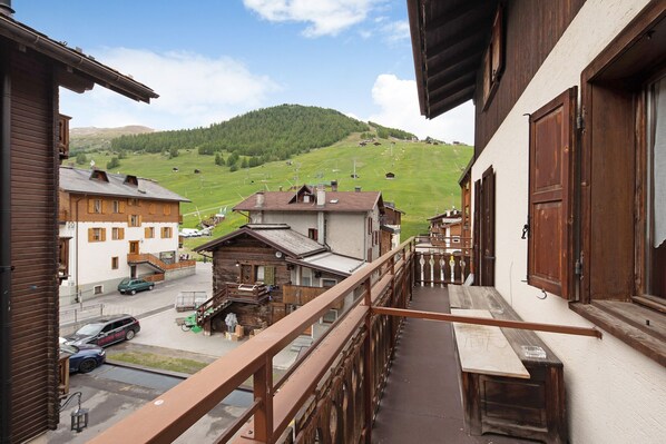 A balcony with a view of a mountain, a wooden house, and a street with parked cars.