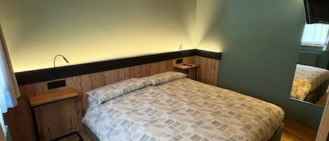 A bedroom with a wooden ceiling, a bed with patterned bedding, a nightstand, and a wall-mounted TV.